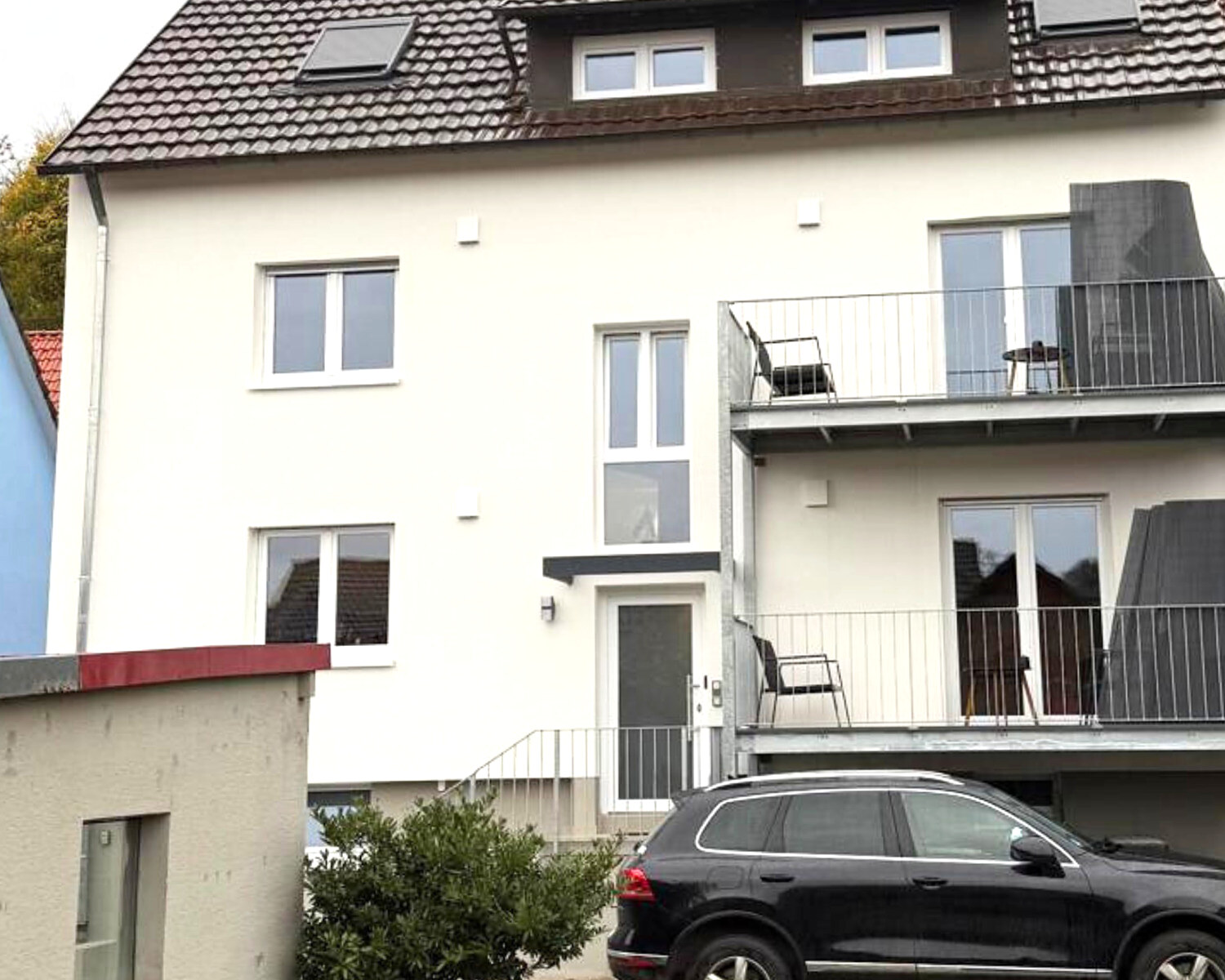 Dasselbe Haus nach der Modernisierung: helle Fassade, neue Fenster, Stahl-Glas-Balkone