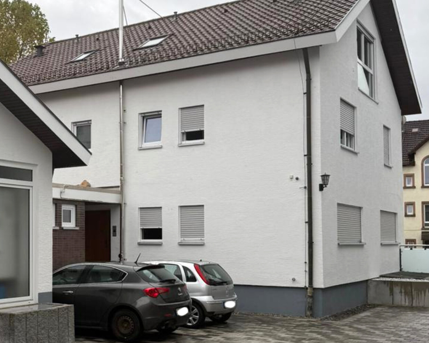 Dieselbe Hofseite nach der Kernsanierung: neues Satteldach, neuer Putz, derselbe Backstein-Windfang